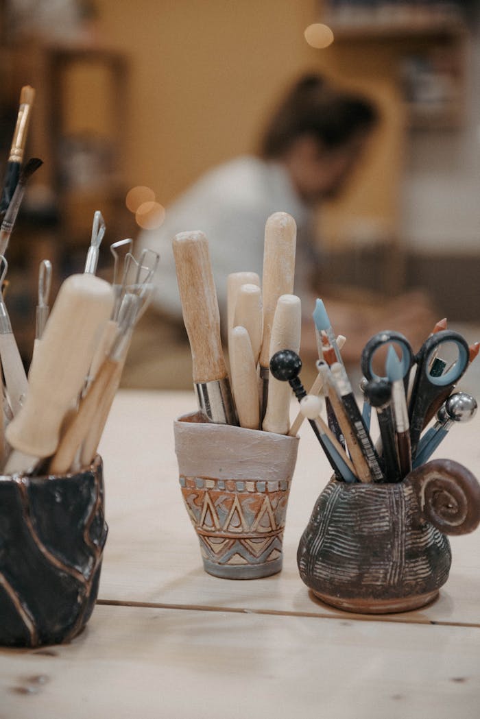 Close-up of assorted artisan tools in decorative ceramic holders inside a workshop.